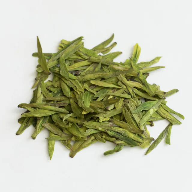 Flat, green Longjing tea leaves arranged on a white surface